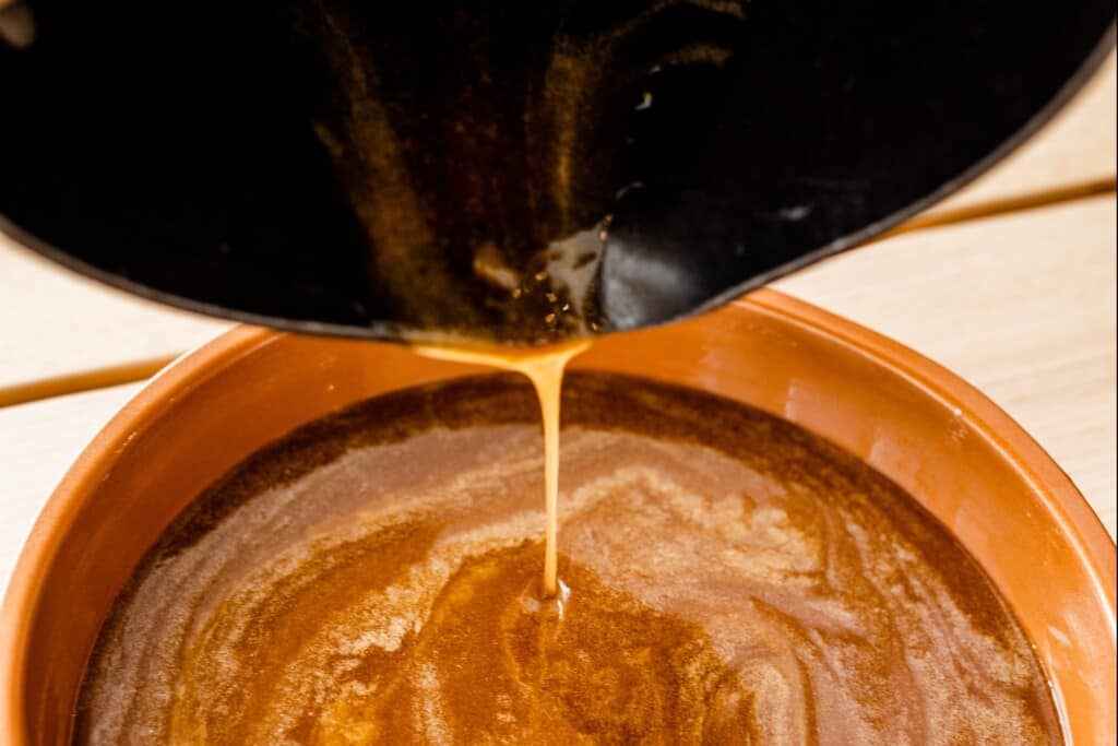Caramel sauce is being poured from a sauce pan in to the greased pie tin.
