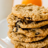 Six freshly baked cookies loaded with orange zest and raisins sit on top of each other on a white platter.