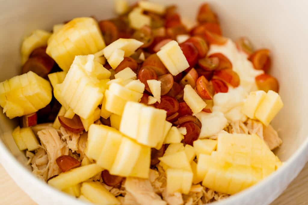 All the ingredients sit in the mixing bowl for chicken salad.