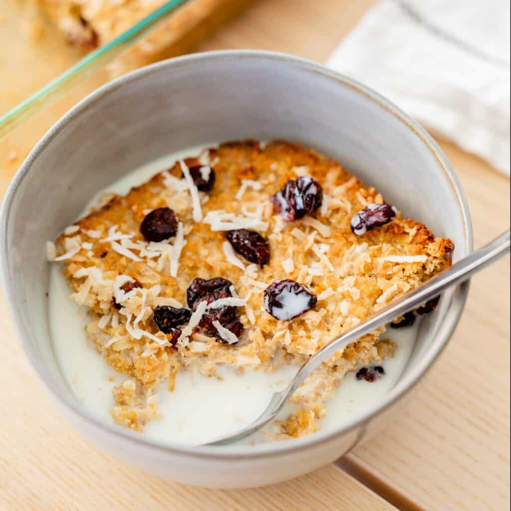 Golden corner piece of baked oatmeal is sitting in a bowl with milk with a spoon.