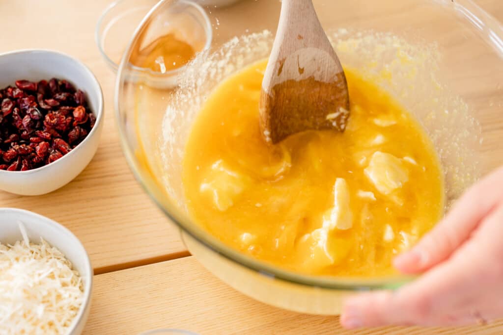 Glass bowl with melted butter being stirred by a wooden spoon.