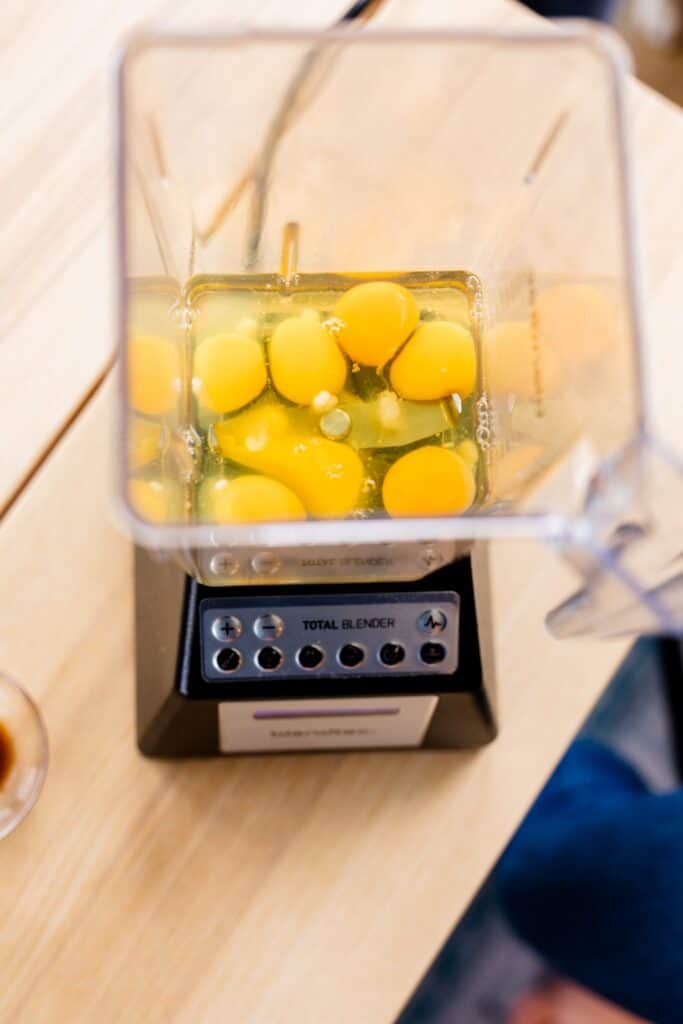 Seven egg whites and yolks sit in the bottom of a blender.