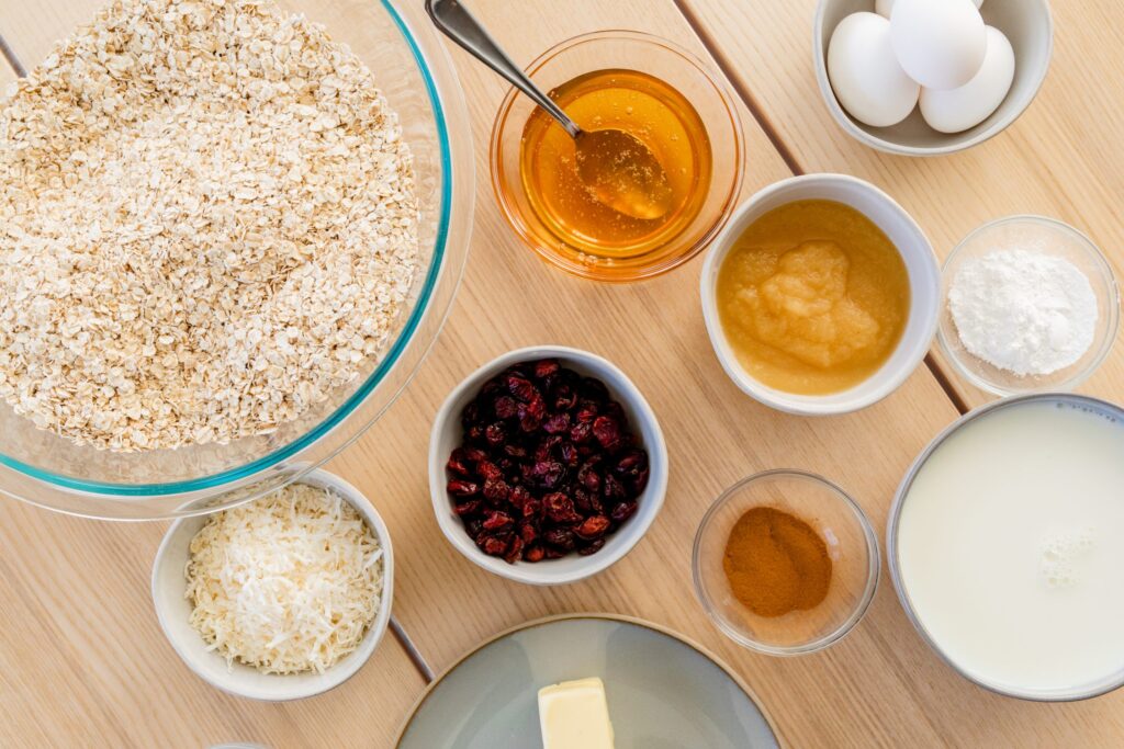 Ingredients for baked oatmeal casserole sit on a wooden counter in individual bowls.
