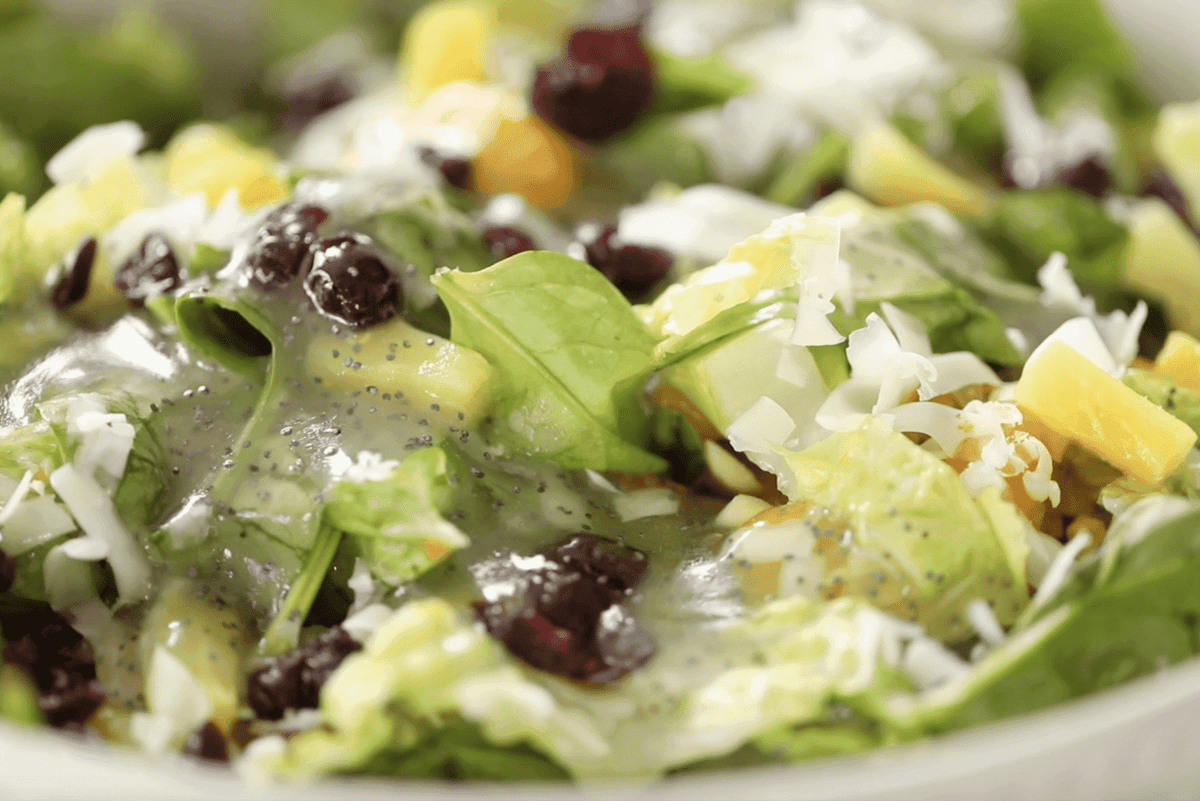 Poppy seed dressing is freshly poured on a fresh salad sprinkled with dried cranberries, swiss cheese, pineapples and mandarin orange wedges.