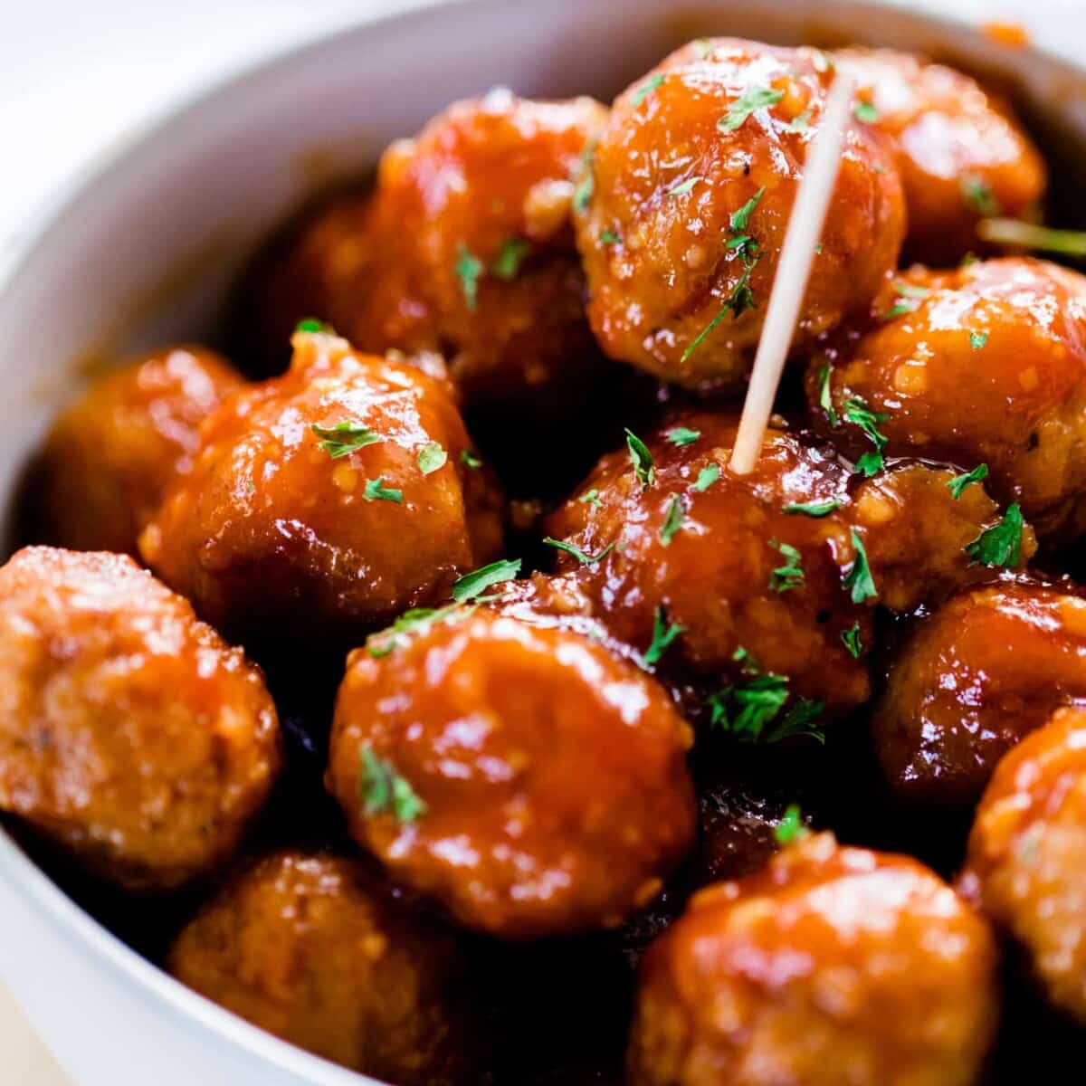 Bowl full of hot meatballs covered in sticky honey garlic glaze is ready to enjoy. A toothpick sits in a meatball in the center of the bowl.