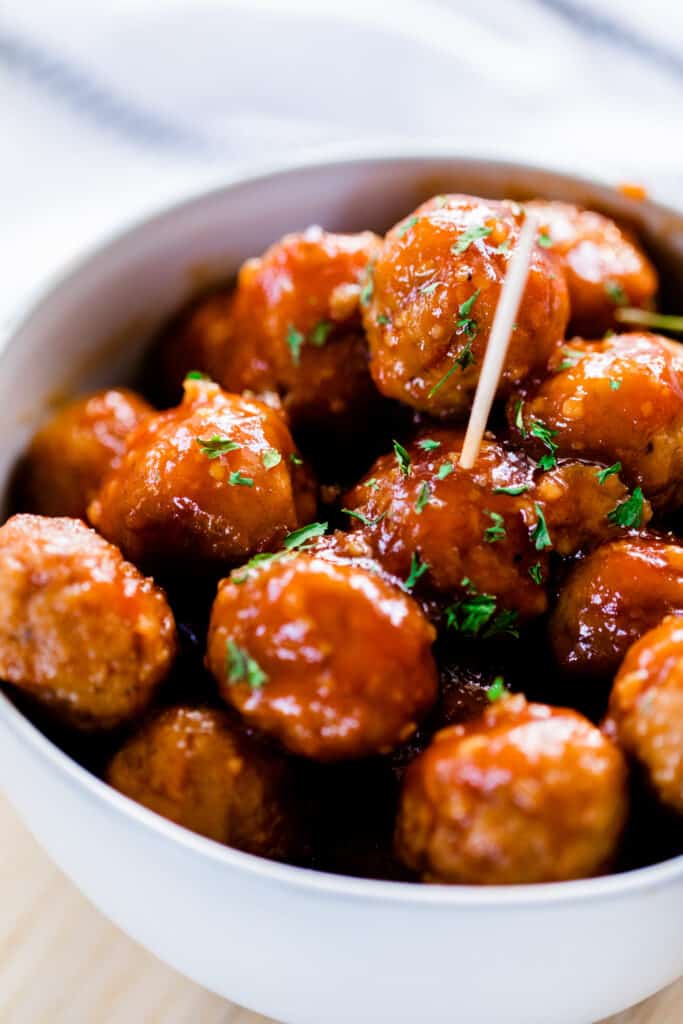 Bowl full of hot meatballs covered in sticky honey garlic glaze is ready to enjoy. A toothpick sits in a meatball in the center of the bowl.