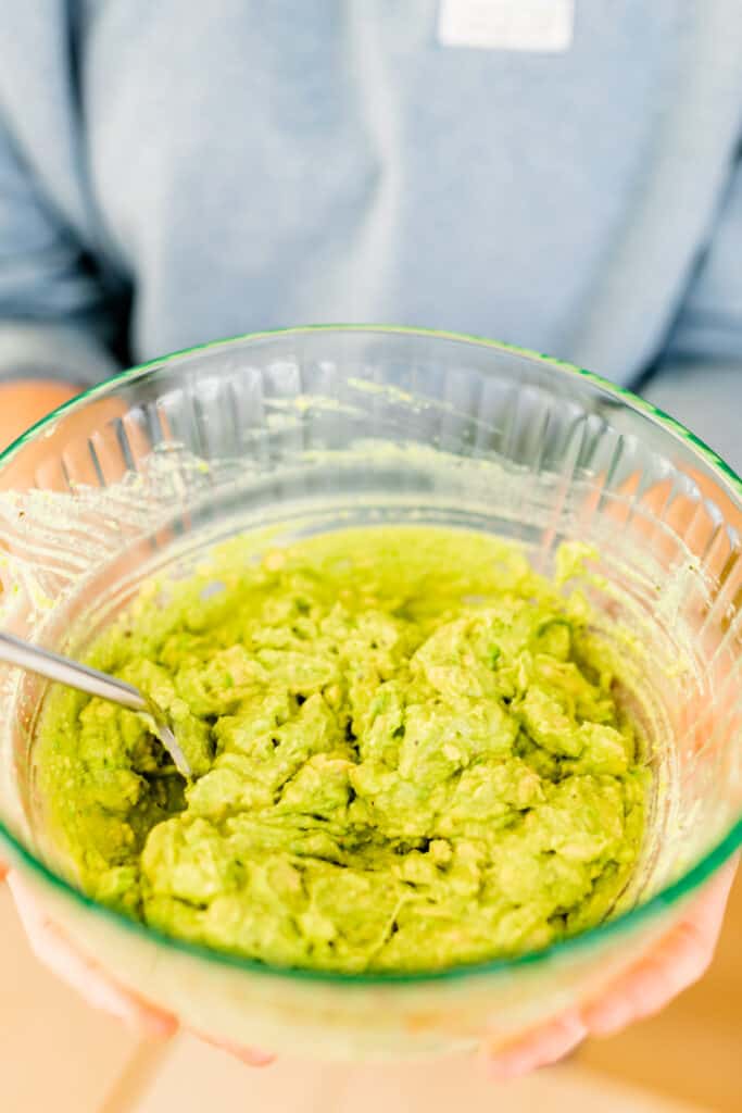 Bowl of guacamole sits in a glass bowl in Ashley's hands.