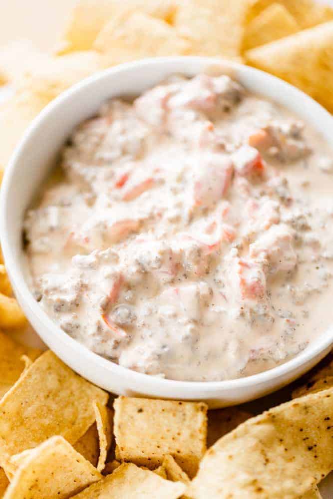 Bowl of creamy sausage rotel dip sits on a table surrounded by tortilla chips ready to enjoy.
