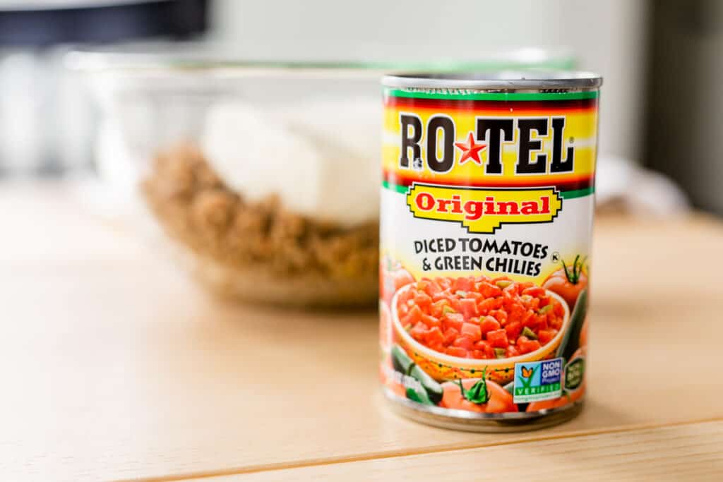 Can of Rotel sits in front of a glass bowl with sausage and cream cheese.