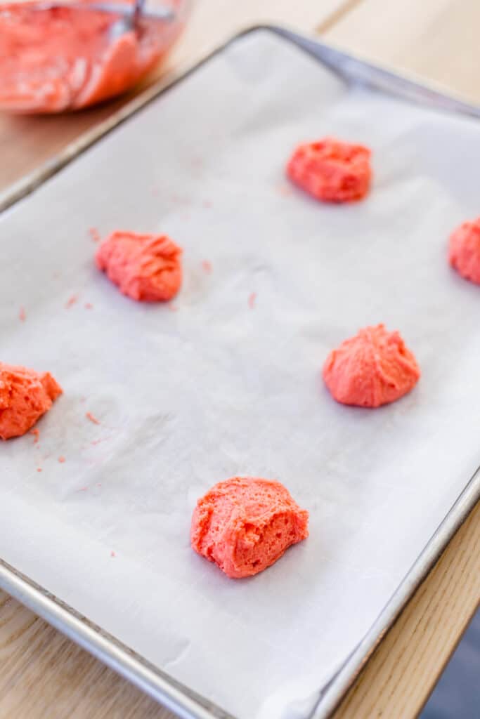 Cookie dough balls sit on top of a piece of parchement paper on top a cookie sheet.