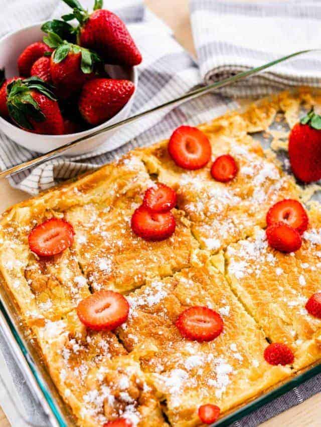 Pan of German Pancakes is topped with powdered sugar and sliced strawberries.