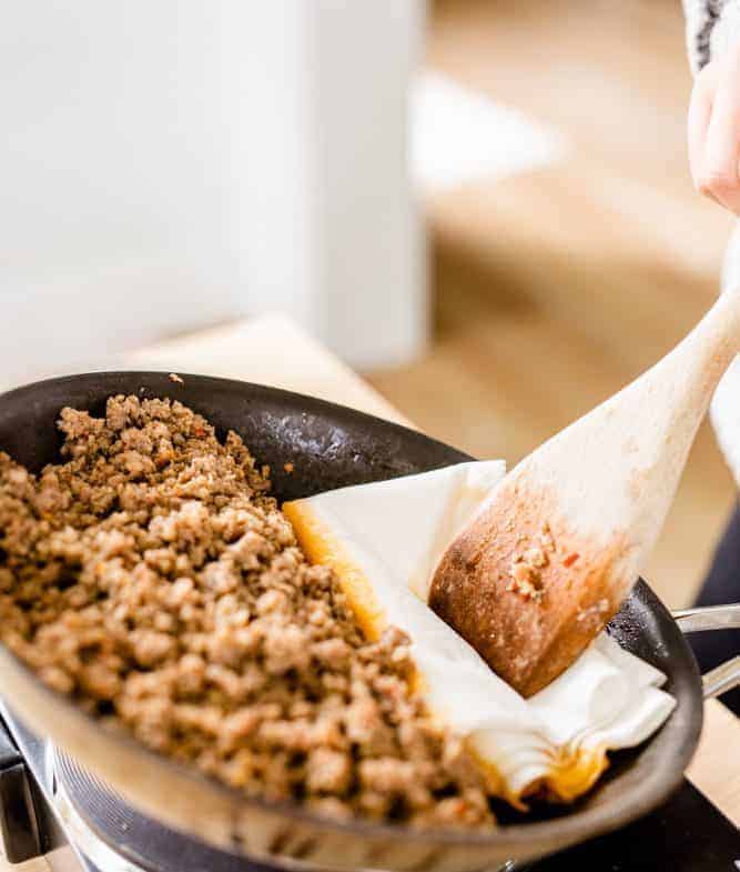 Grease is being removed from skillet where sausage cooked with a paper towel.