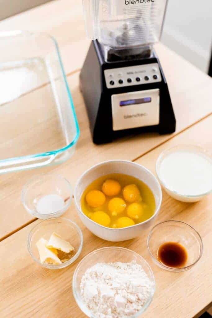 Ingredients for German Pancakes sit on table with blender and glass pan behind.