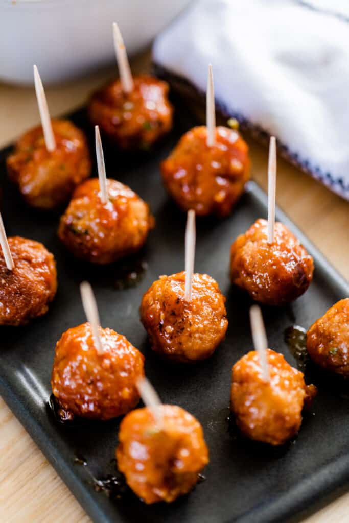 A rectangular plate sits on a table filled with honey garlic meatballs. Each meatball has a toothpick in the center for passing.