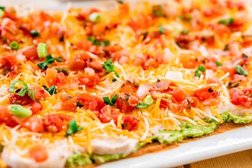 Best seven layer Mexican dip sits on a platter ready to be scooped up and enjoyed.