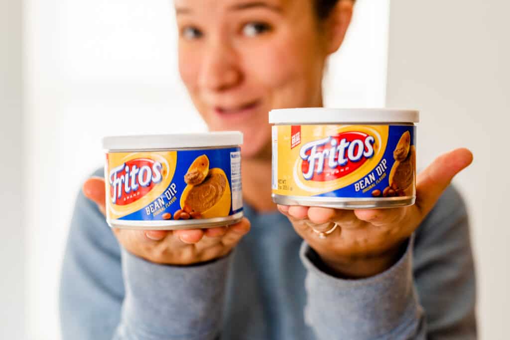 Ashley holds two small cans of Fritos brand bean dip.
