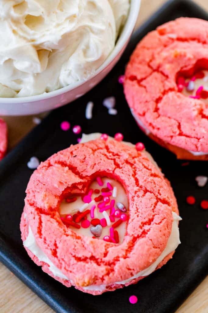 Pink Valentine cookie sandwiches sit on a plate with heart cut-outs on top.