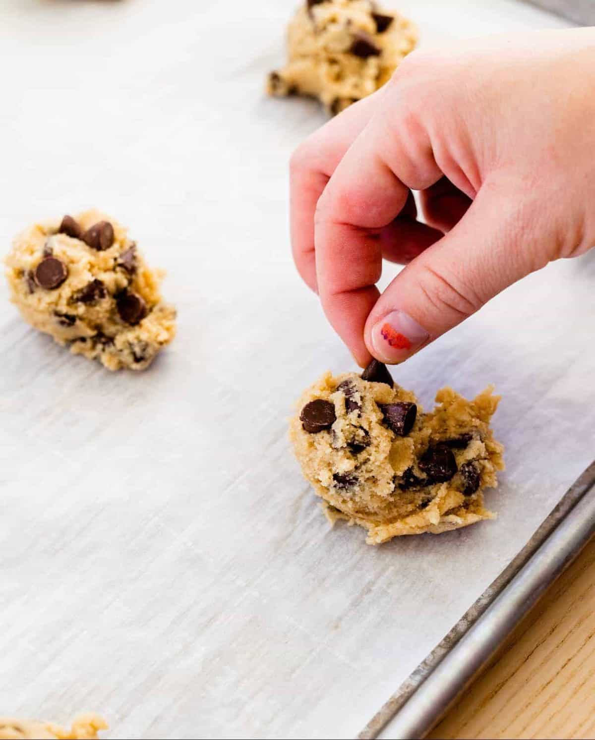 Balls of cookie dough sit on a baking sheet topped with extra chocolate chips.