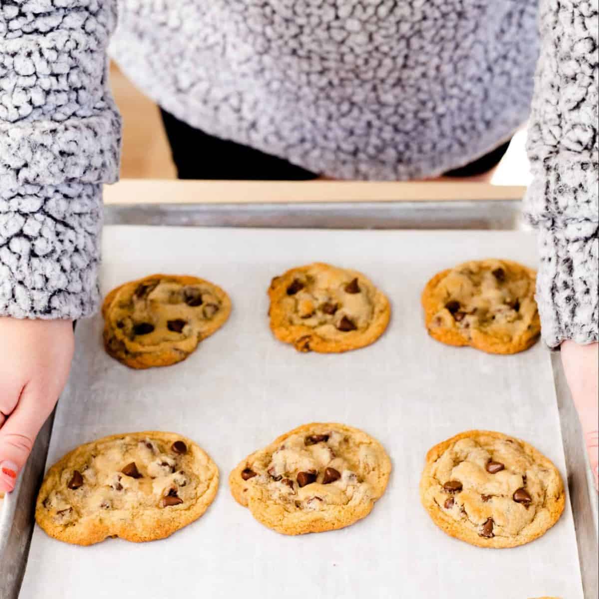 Ashley holds a baking sheet with 9 perfectly golden chocolate chip cookies.