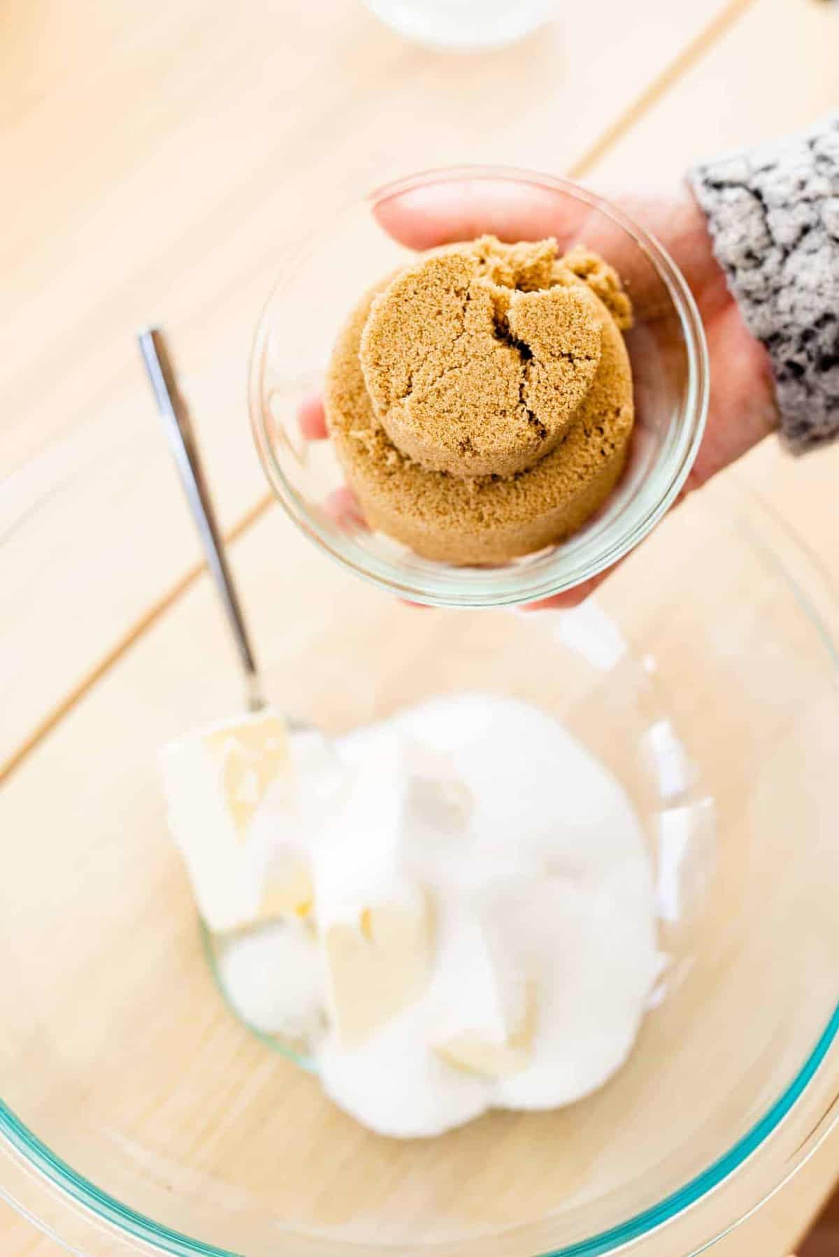 Ashley holds a small bowl of brown sugar over a bowl with cubed butter, and sugar.