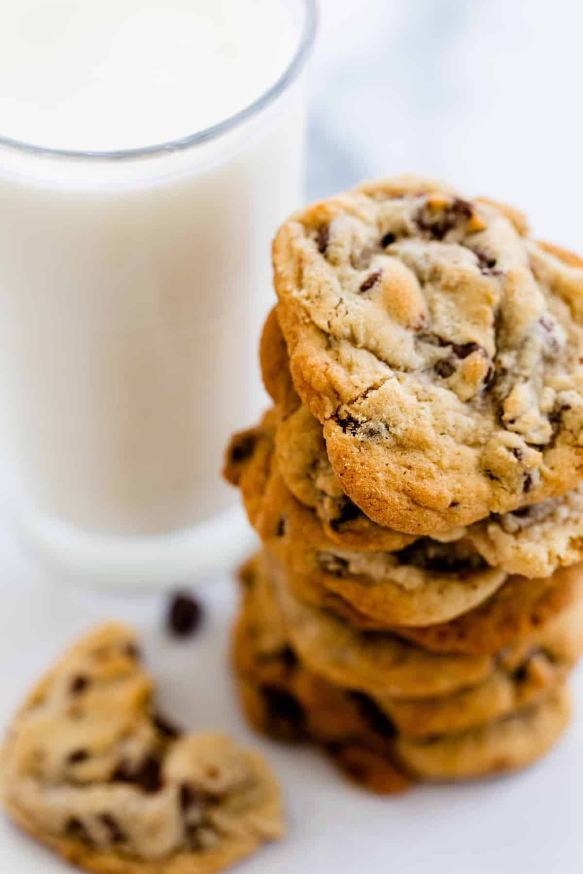 A tall stack of chocolate chip cookies sits next to a glass of milk.