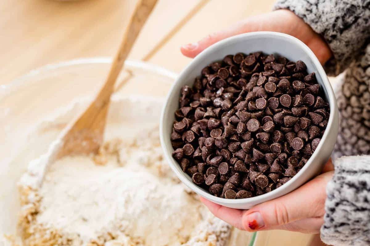 Ashley holds a bowl of chocolate chips over the dough mixture and remaining flour.