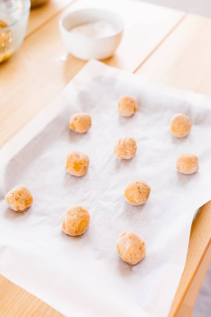 Cookie dough balls sit on a baking sheet covered with parchment paper, ready to go in the oven.