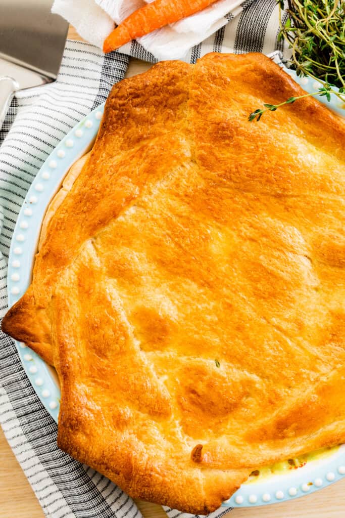 A beautiful golden brown Chicken Pot Pie in a pie dish is ready to slice and serve.
