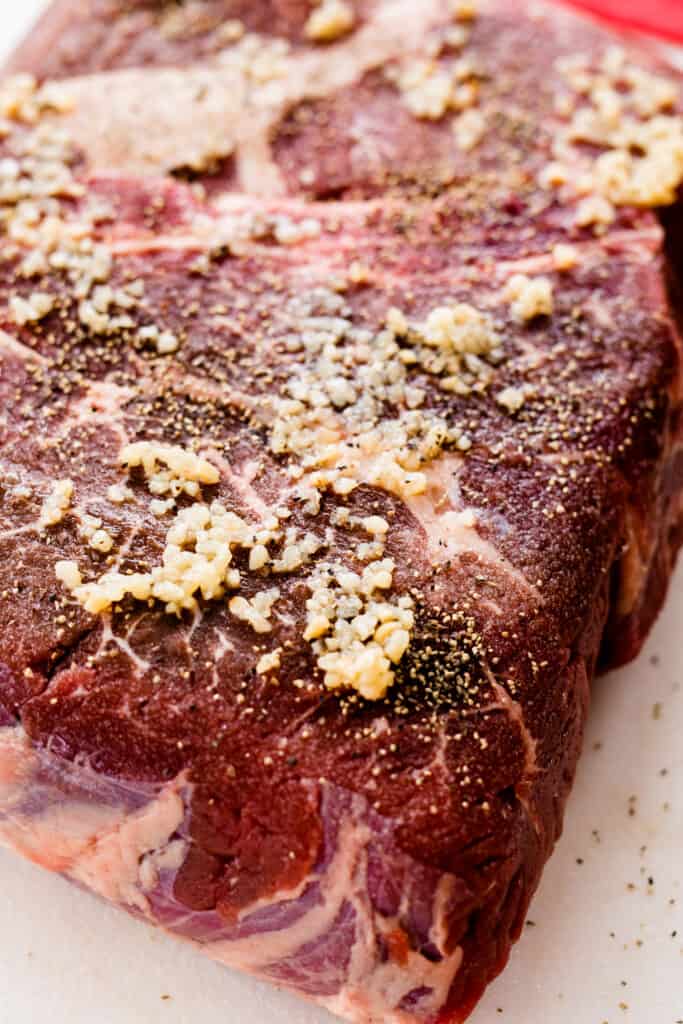 A well seasoned chuck roast is covered with salt, pepper and minced garlic.