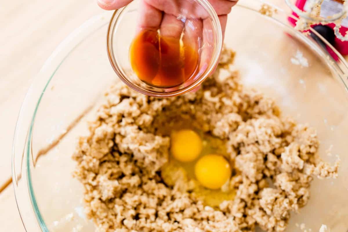 Ashley holds a small bowl of vanilla over a bowl with creamed butter, sugar and eggs.