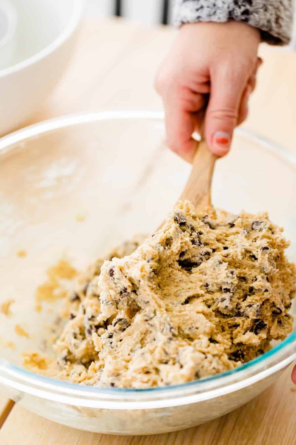 A wooden spoon gently folds in the last of the flour and chocolate chips.