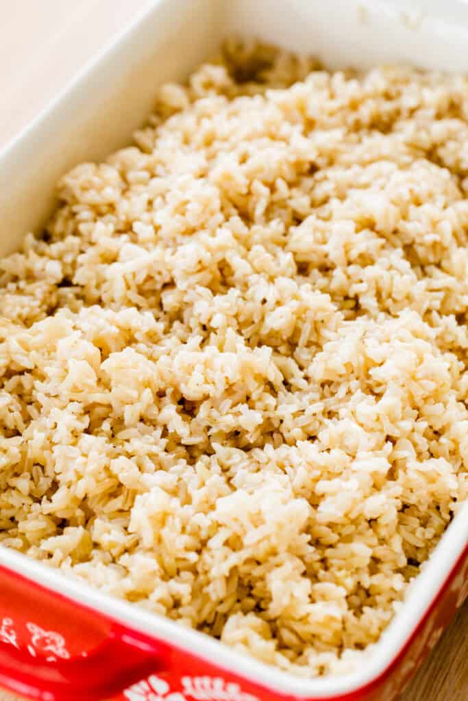 Red ceramic casserole dish is filled with brown rice, perfectly cooked and ready to eat.