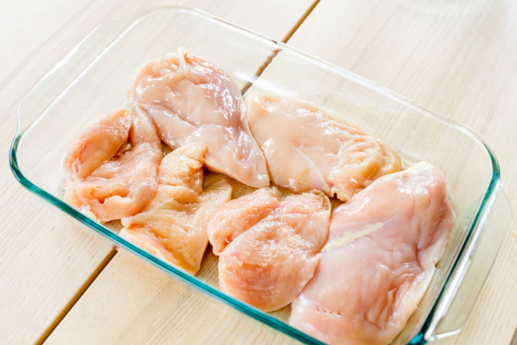 Chicken breasts sit in a glass casserole dish ready for layering.