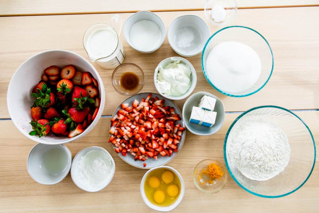 Ingredients for strawberry cake sit on a table top in small individual bowls.