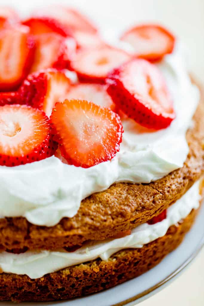 Strawberry Layer Cake sits on counter topped with fresh sliced strawberries.