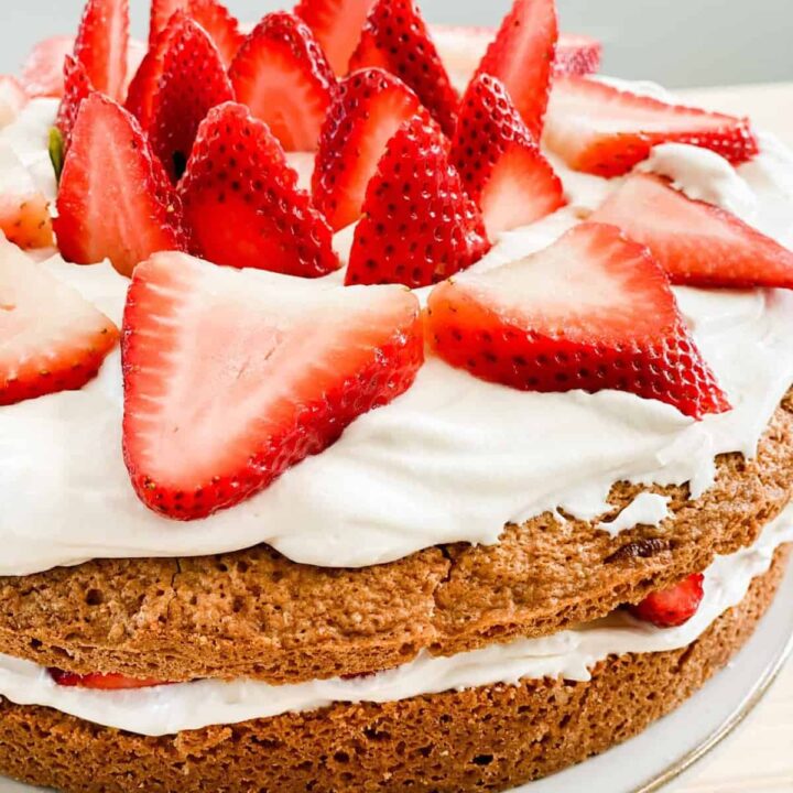 Freshed sliced strawberries decorate the top of a 2 layered cake.