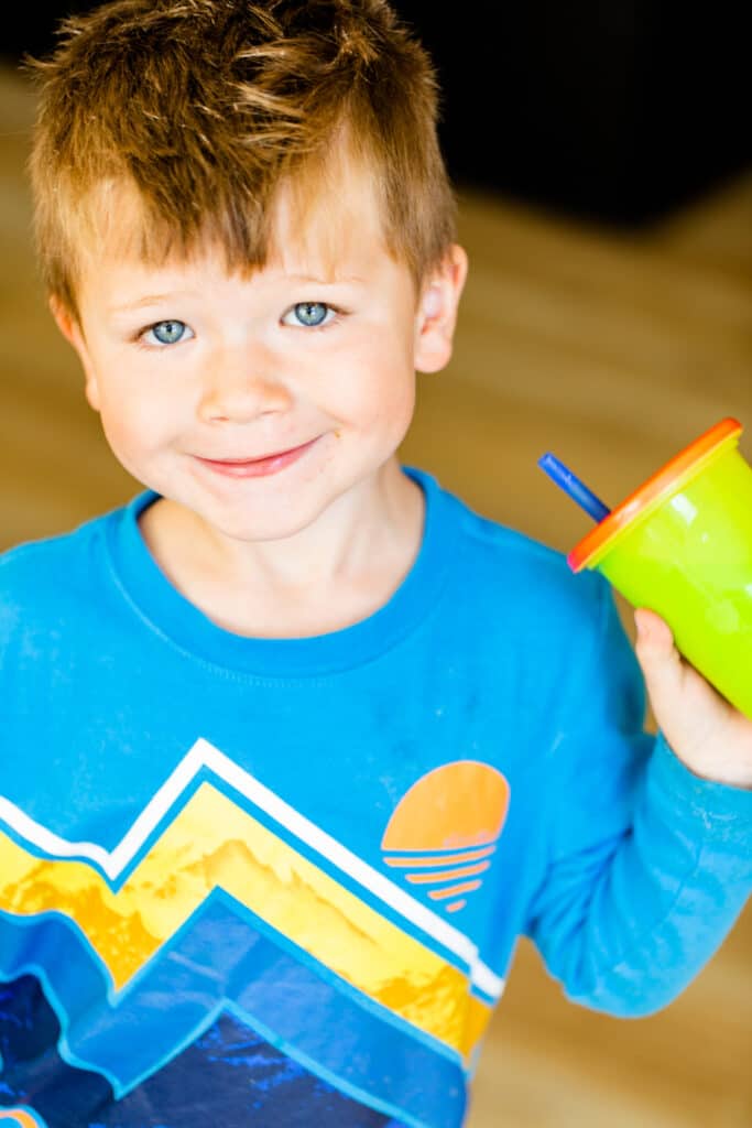 George is wearing a bright blue shirt and holding a cup with straw. His cup is filled with a bright green smoothie.