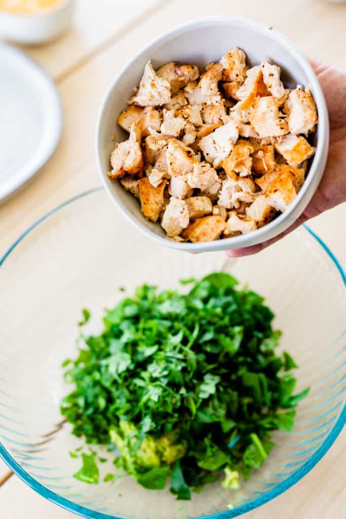 Grilled chicken is held in a small white bowl over the top of a bowl with cilantro and spinach.