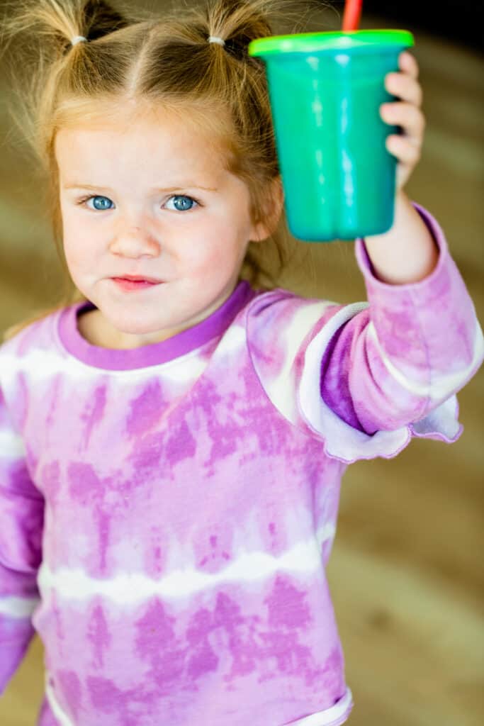James is wearing a purple tie-dye shirt and holding a cup with straw. Her cup is filled with a bright green smoothie.