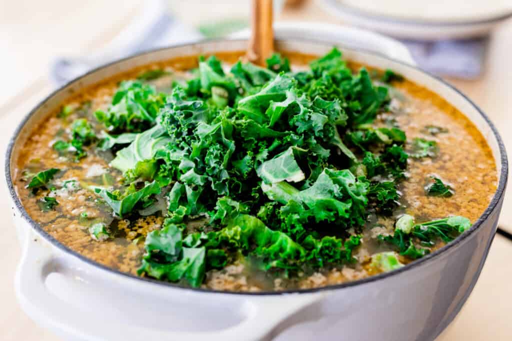 Chopped, vibrant green kale sits on top of the soup in the lodge pot.