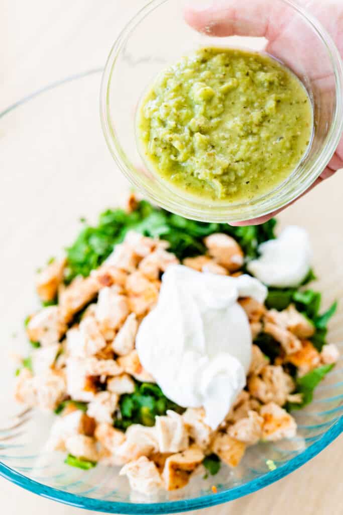 Small bowl of salsa verde is held over larger bowl of ingredients.