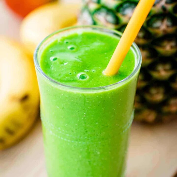 Vibrant green smoothie fills a tall glass cup. A yellow straw sits in the smoothie.