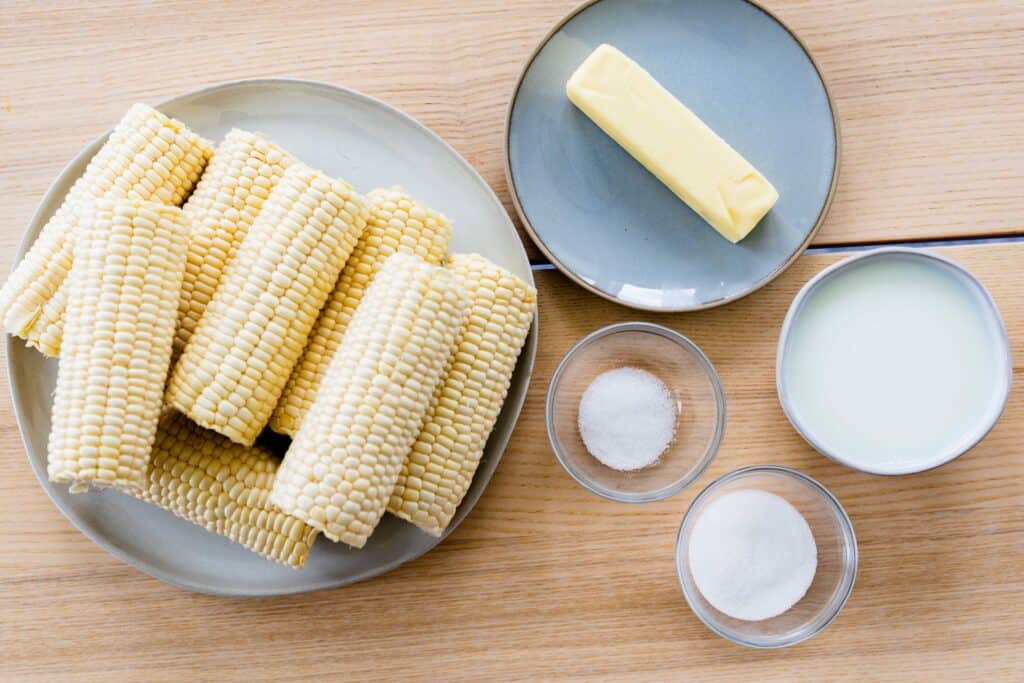 Ingredients for corn on the cob sit on counter, Husked corn, stick of butter, salt, sugar and milk.