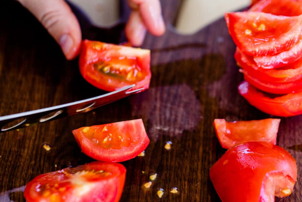 Ashley holds a knife while she removes the center of red plump tomatoes.