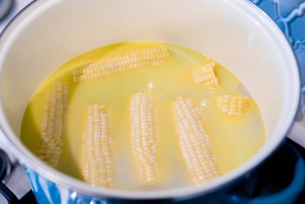 Six cobs of corn float in a large ceramic pot of boiled water, milk and butter.