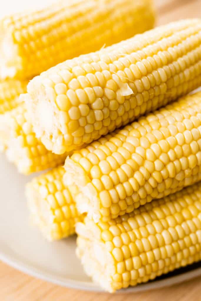 Cooked cobs of corn sit on a white plate, stacked in a pyramid.