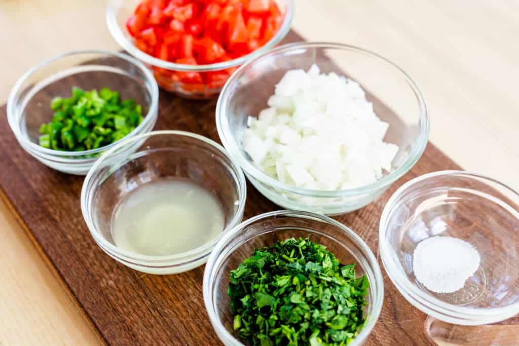All the ingredients for salsa fresca sit on a chopping board ready to be combined.