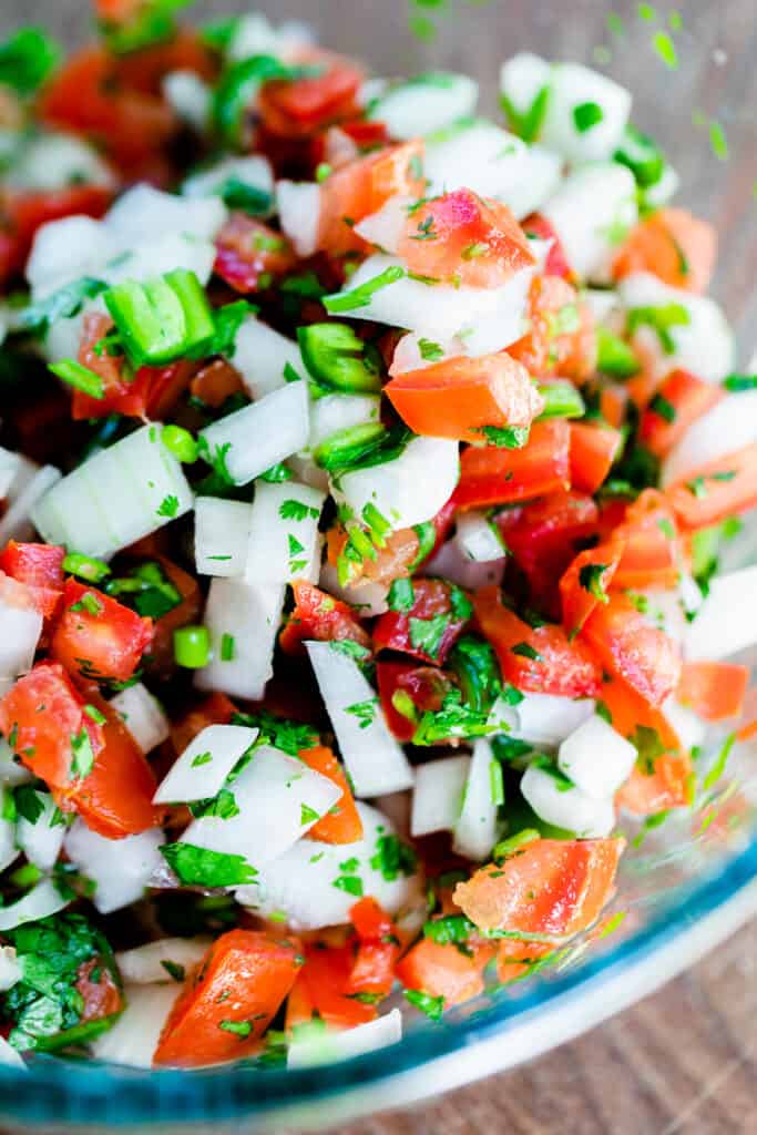 Colorful Pico de Gallo sits in a glass bowl, mixed and ready to chill.