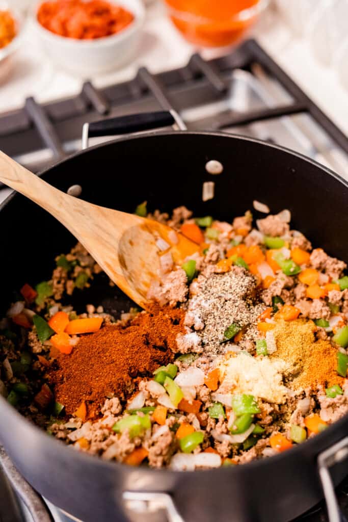 Seasonings are added to large black pot of veggies, beans and beef.