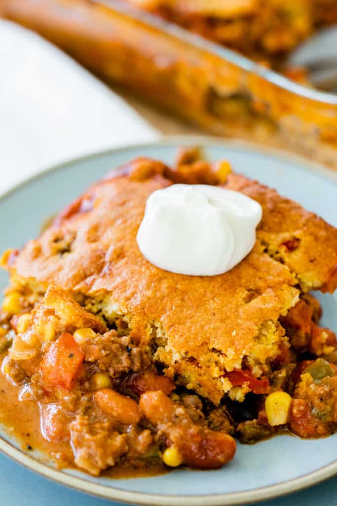 Serving of tamale pie sits on a plate ready to eat, garnished with sour cream.